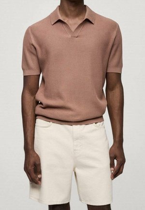 Man met een bruine, gestructureerde polo met korte mouwen gecombineerd met crèmewitte knielange korte broek tegen een effen achtergrond.