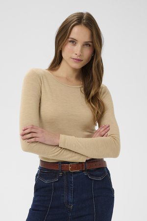 Bēša garām piedurknēm topiņš ar apaļu kakla izgriezumu, izgatavots no mīksta, ribota auduma. Kombinēts ar tumšu džinsa svārku un brūnu ādas jostu.