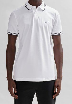 Mand iført hvid polo-shirt med sortstripet krave og ærmer samt "BOSS" logo på venstre bryst, kombineret med sorte bukser.