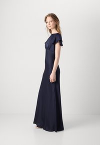 Rochie lungă, de un albastru marin, cu mâneci scurte volă pentru un aspect elegant și un corset ajustat, având o textură de material neted și fluid.