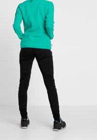 Zwarte leggings en een turkooise fleecejack, getailleerd met lange mouwen en textuurstof, gecombineerd met zwarte sportieve schoenen.