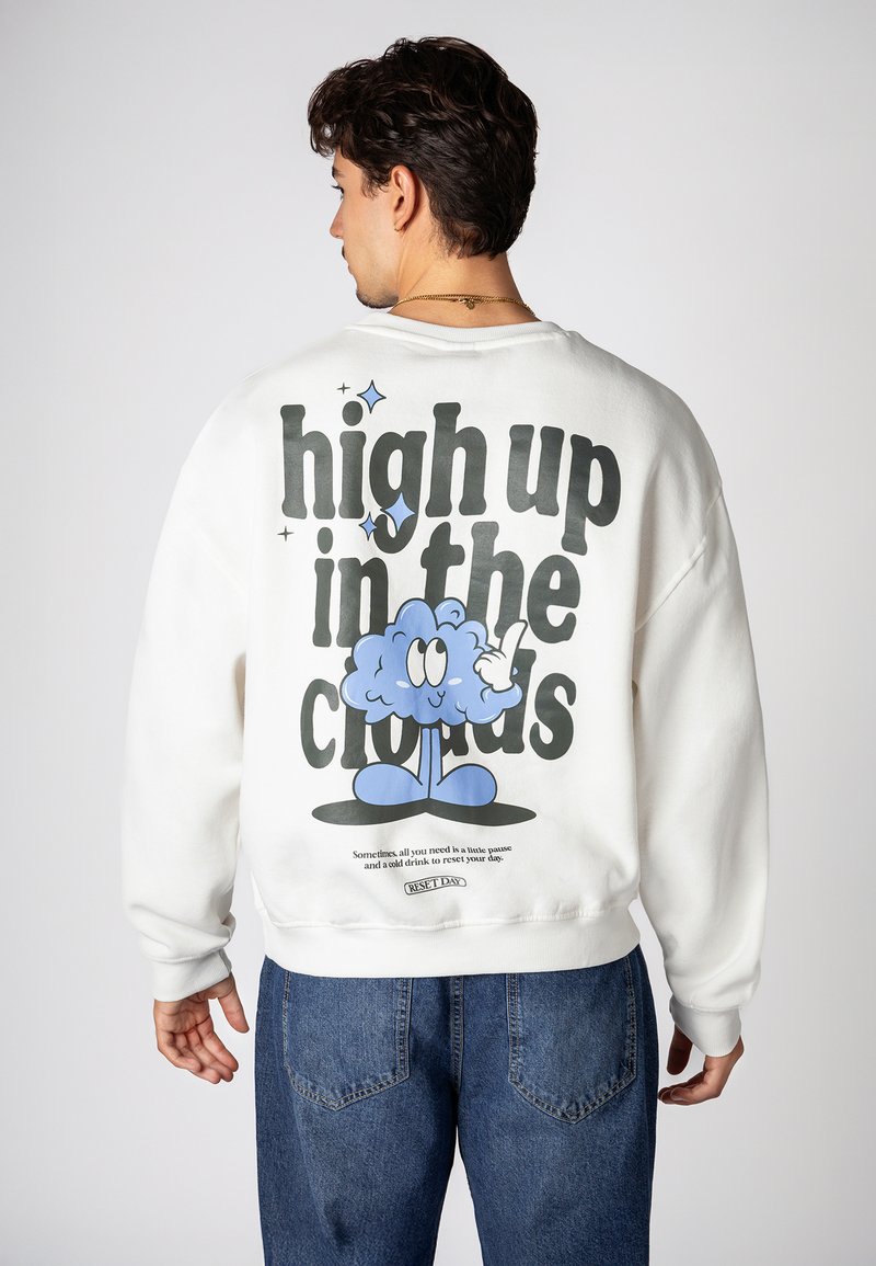 Weißer Sweatshirt mit einem Grafikdruck auf der Rückseite, der den Text "hoch in den Wolken" und eine Cartoon-Wolkenfigur zeigt. Lockerer Schnitt.