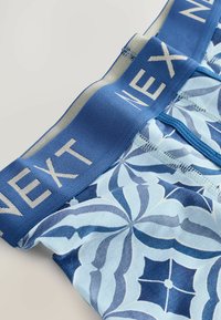 Des boxers pour hommes avec une ceinture élastique bleue arborant le logo "NEXT", et un motif floral bleu clair sur un fond en tissu doux.