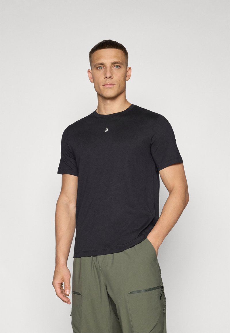 Sort kortermet t-shirt lavet af blødt materiale, med rund halsudskæring og et lille hvidt logo på brystet. Kombinationen er med olivengrønne shorts.