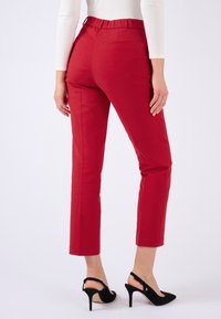 Pantalones rojos de corte entallado con ajuste slim, que presentan una cintura alta y bolsillos traseros. Combinados con tacones stilettos negros, mostrando una silueta elegante.