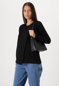 Pull en tricot noir avec un col rond, associé à un jean en denim bleu clair, tenant un sac à main structuré noir avec une courte bandoulière.