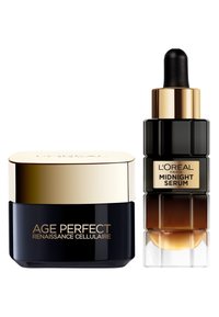 Le set de soins L'Oréal Paris comprend un pot noir avec un couvercle doré étiqueté "Age Perfect" et une bouteille compte-gouttes noire et texturée étiquetée "Sérum de Minuit".