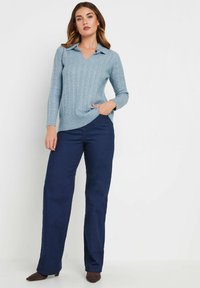 Ljusblå stickad tröja med V-ringning och krage, med ett strukturerat kabelmönster. Bärs med mörkblå vida byxor.