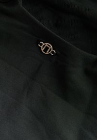 Crna tkanina s teksturiranim završetkom, s malim zlatnim metalnim detaljem u obliku kruga i navojnim dekorom.