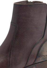 Bota de tobillo de cuero marrón con un acabado texturizado, que presenta un sutil patrón de reptil en el costado y un tacón de madera bajo.