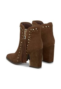 Stivaletti alla caviglia in suede marrone con tacco spesso, decorati con borchie e una nappina ornamentale, dotati di chiusura con zip laterale.