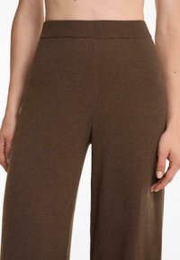 Pantaloni a gamba larga marroni realizzati in un morbido tessuto a maglia testurizzata con una vita elastica. Il design è semplice e lineare, senza dettagli aggiuntivi.