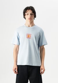 Lichtblauw katoen t-shirt met korte mouwen en een ronde hals, met in het midden de tekst "FEED YOUR MIND" in rood en oranje.