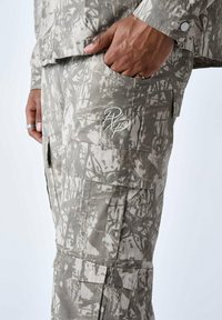 Cargo-broek in een grijs en beige abstract patroon, gemaakt van ademende stof. Heeft meerdere zakken en een geborduurd logo-detail.