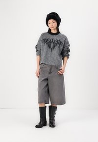 Grijze wollen trui met een donker textuurpatroon, grijze denim culottes en kniehoge matte zwarte laarzen met gespen, tegen een witte achtergrond.