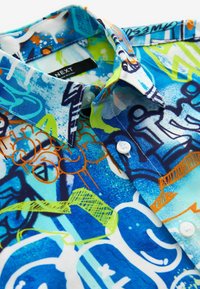 Kurzarmhemd mit einem mehrfarbigen Graffiti-Druck in Blau, Grün und Orange. Verfügt über einen Button-Down-Kragen und weiße Knöpfe.