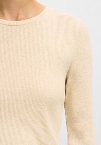 Beige, geripptes Langarmshirt mit rundem Halsausschnitt. Der Stoff wirkt weich und hat eine feine Textur. Nahtdetails sind an der Schulter sichtbar.