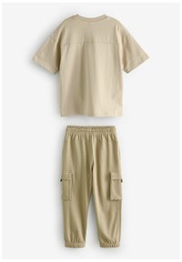 Beigefärgad t-shirt med kort ärm och matchande cargobyxor i mjukt material, med elastisk midja och sidofickor.