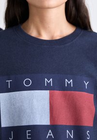 Camiseta de algodón azul marino con un gráfico que presenta bloques rectangulares en rojo y azul claro y texto blanco que dice "TOMMY JEANS".