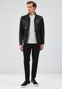 Zwart leren jack met voorzakken, grijs t-shirt met ronde hals, zwarte slim-fit broek en zwarte sneakers met witte zolen. Eenvoudig ontwerp.