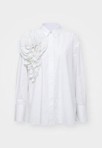 Camicia bianca con colletto a bottoni, caratterizzata da un design plissettato e testurizzato sulla spalla sinistra. Maniche lunghe con polsini abbottonati, realizzata in tessuto morbido.