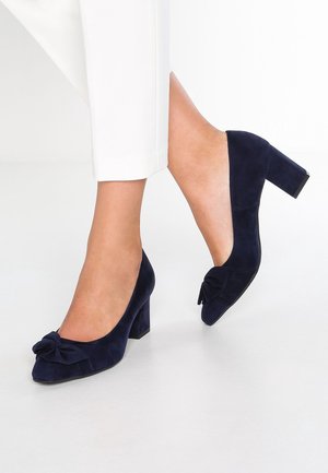 Navy blue suede block-heeled pumps with a pointed toe and a decorative bow on the front. Smooth texture and sturdy base for support.