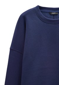 Granatowy sweter z okrągłym dekoltem, żebrowanymi mankietami i miękką teksturą. Posiada wzmocnione szwy na ramionach dla większej trwałości.