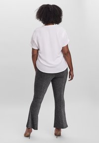 Weißes kurzärmeliges T-Shirt mit umgeschlagenen Ärmeln, kombiniert mit eng anliegenden schwarzen, strukturierten Schlaghosen. Modell trägt beigefarbene High Heels.
