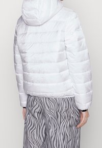 Vit pufferjacka med horisontell sömnad och huva, med en slät textur. Matchad med grå byxor i zebramönster.