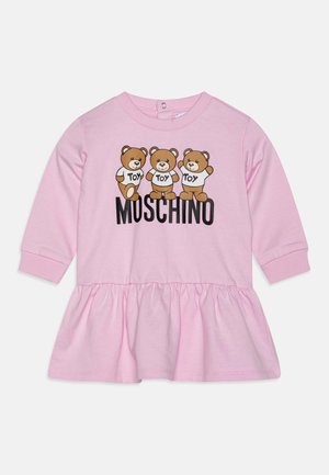 Jasnoróżowa sukienka niemowlęca z długim rękawem, na której znajdują się trzy misie w koszulkach z napisem "Toy" oraz napis "Moschino" pod misiami z przodu.