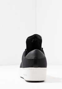 Baskets noires avec une tige en tissu texturé, un arrière lisse et une semelle plateforme blanche. Le design du talon est minimaliste sans logos visibles.