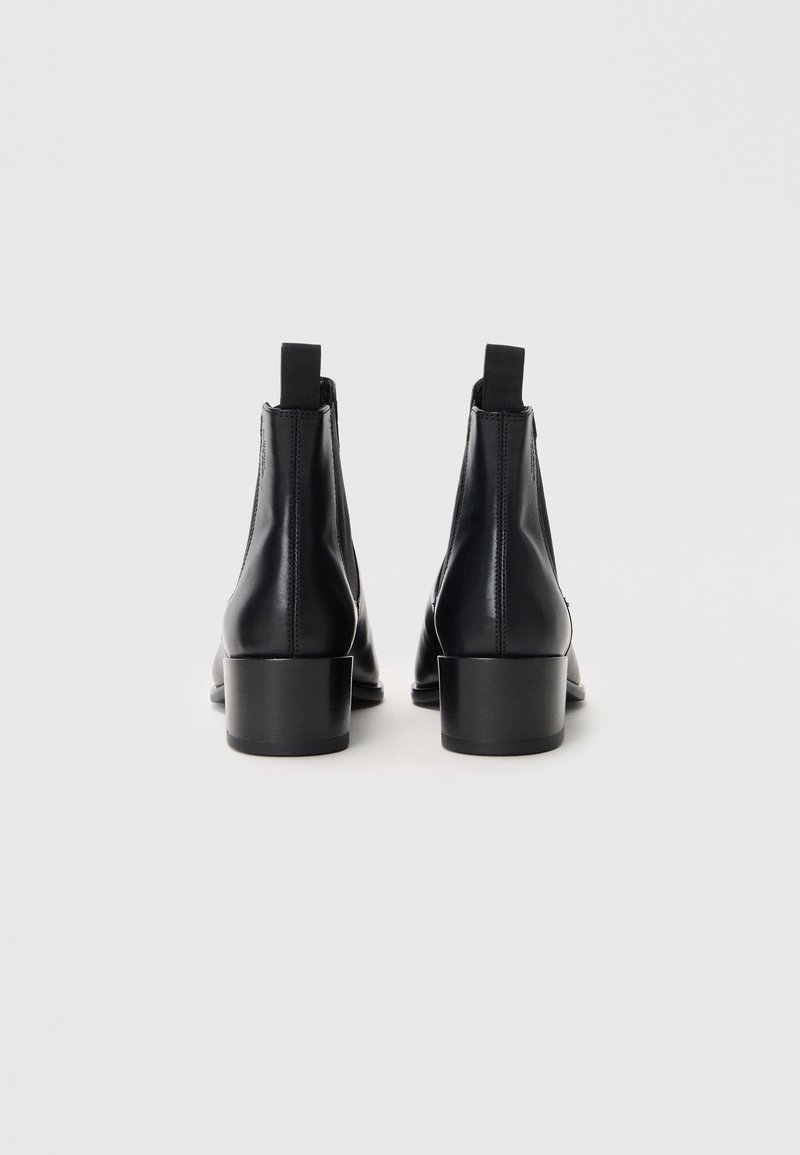 Bottines en cuir noir avec un petit talon carré et des panneaux élastiques sur les côtés. Texture lisse avec peu de coutures, dotées de tirettes.