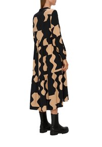 Abito lungo nero e beige con motivo ondulato, orlo a strati e maniche lunghe. Abbinato a stivaletti neri alla caviglia. Tessuto dalla superficie liscia.