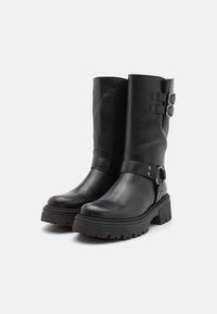 Botas de cuero negras hasta el tobillo con una suela gruesa, que cuentan con dos correas ajustables con hebillas y un acabado suave.
