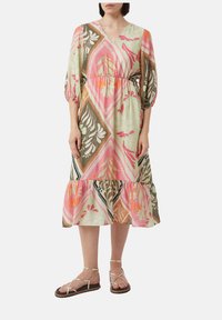 Sukienka w kwiatowy wzór w pastelowej zieleni, z dekoltem w kształcie litery V, bufkami, talią ściągniętą oraz warstwowym dołem z falbaną. Noszona z sandałami na ramiączkach.