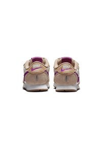 Zapatillas Nike con parte superior en tonos beige y blanco, acentos morados, textura de ante y una suela acolchada con una unidad de aire visible en el talón.