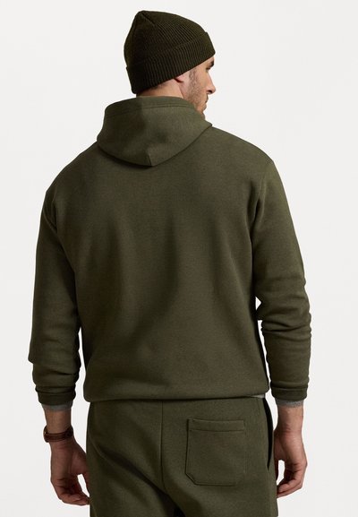 Ελιά πράσινη φόρμα με κουκούλα και κορδόνι, με ραμμένα μανίκια και λεπτομέρειες τσέπης. Μαλακό ύφασμα, εφαρμοστή σχεδίαση, φορεμένη με ταιριαστά παντελόνια.