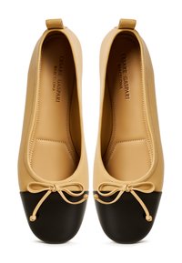 Ballerine con tomaia color tan e punta rotonda nera, con un dettaglio a fiocco nella parte anteriore. Realizzate in pelle liscia con finitura opaca.