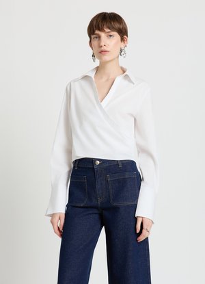 White wrap shirt with a V-neck, long sleeves, and extra-long cuffs, paired with wide-leg dark blue denim jeans with front pockets.