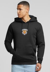 Čierna mikina s kapucňou vyrobená z mäkkého materiálu s prednou kapsou, s logom Detroit Tigers a grafikou tigra na hrudi.