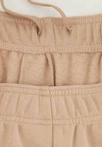 Pantalones de chándal beige con un interior suave, cinturilla elástica y cordón. La tela tiene una textura lisa con detalles de costura visibles.