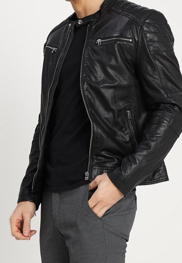 Svart lädermotorcykeljacka med dragkedjefickor, kviltade axlar och en figursydd design. Åtföljd av en svart topp och texturerade grå byxor.