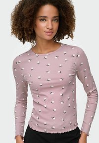 Długi rękaw, dopasowany top w miękkim różowym prążkowanym materiale z białym kwiatowym wzorem i postrzępionym dołem. Okrągły dekolt z delikatnym wykończeniem.