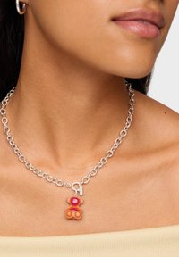 Collana con catena d'argento con ciondolo a forma di orso colorato in tonalità di rosa, arancione e rosso, che aggiunge un elemento di design giocoso.
