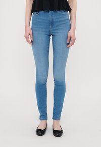 Høytlivs slim-fit jeans i lyseblå denim. Har fem lomme-design og subtil falming. Kombinert med svarte leiligheter og en svart topp.