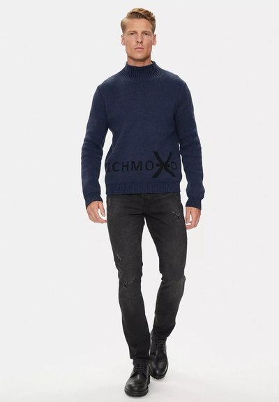 Maglione in maglia blu navy con colletto alto e logo nero "RICHMOXD" in vita. Abbinato a jeans neri strappati e stivali neri.