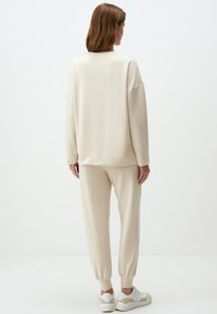 Lichtbeige sweatshirt en bijpassende jogger set gemaakt van een zachte, textuurstof. Sweatshirt heeft een verlaagde schouderlijn; de joggers hebben elastische boorden.