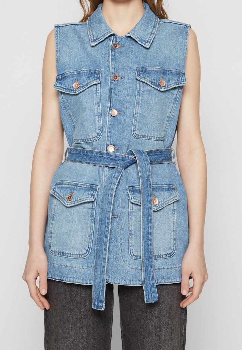 Veste sans manches en denim bleu clair avec quatre poches à rabat devant, fermeture par boutons, col pointu et ceinture en denim assortie nouée à la taille.