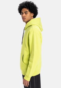 Bright lime green hoodie with a drawstring hood, kangaroo pocket, and ribbed cuffs, featuring a textured finish and minimal design.