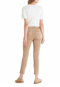 Lichtbruine skinny jeans met een middelhoge taille, achterkantzakken en subtiele stiksels, gecombineerd met een wit t-shirt en beige sneakers.